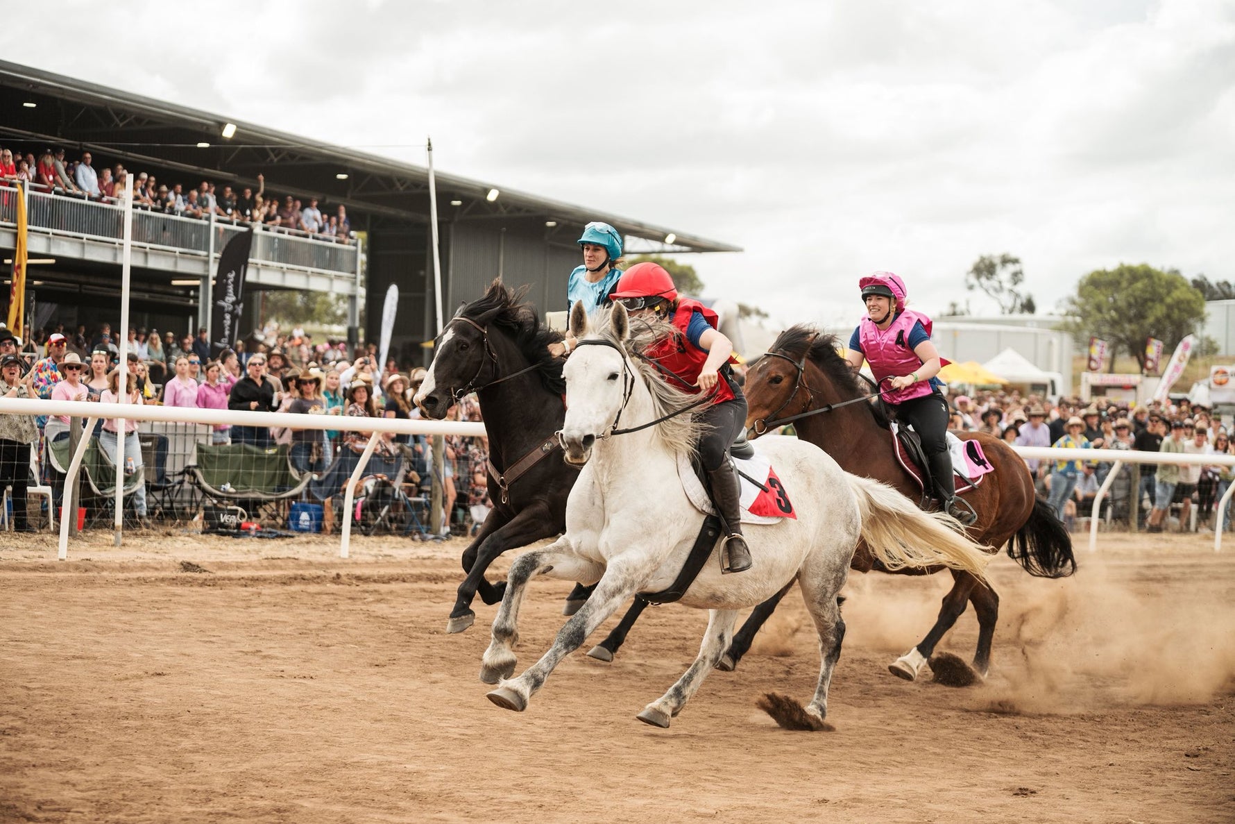 Horses racing on a dirt track with jockeys and spectators in the background.